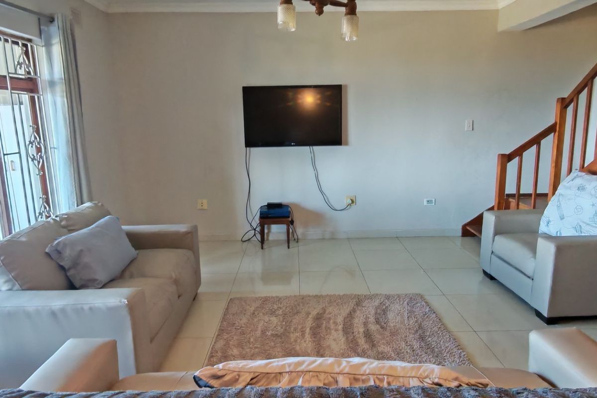 A living room featuring tiled flooring, a wooden staircase, and a security gate, providing a functional space with potential for aesthetic updates.