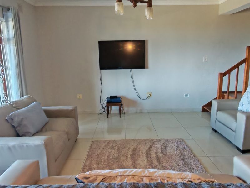 A living room featuring tiled flooring, a wooden staircase, and a security gate, providing a functional space with potential for aesthetic updates.