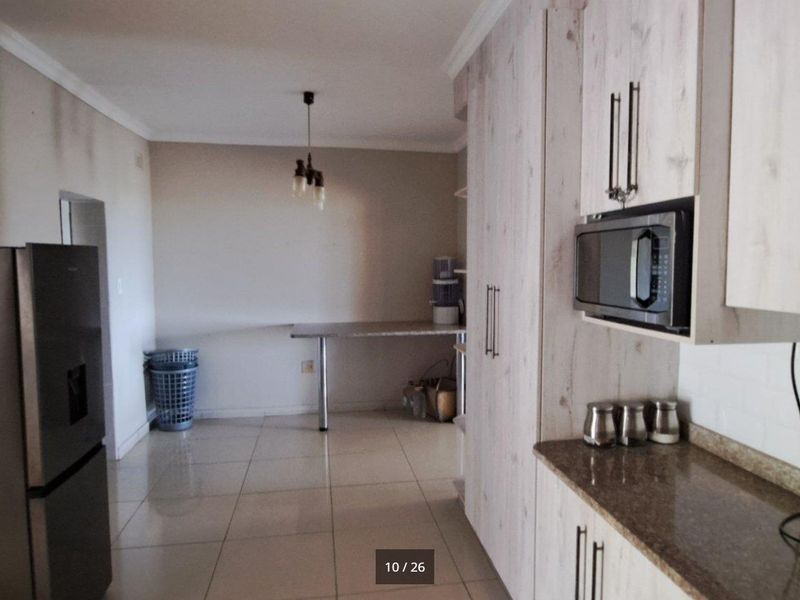 Kitchen area featuring light wood-look cabinetry, granite countertops, built-in microwave, and tiled flooring, with some visible wall wear requiring maintenance.
