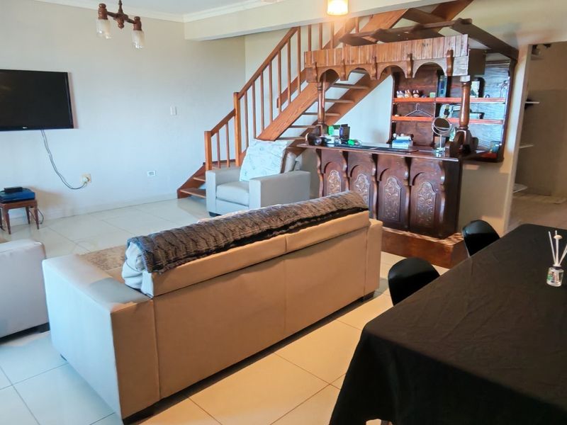 Open plan living area featuring tiled flooring, a wooden staircase, and a built-in bar unit, providing a functional layout for entertaining.