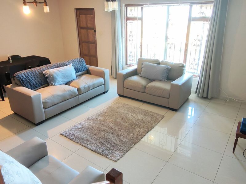 Open-plan living and dining area featuring neutral tiled flooring, large windows with security gates, and direct access to the exterior.