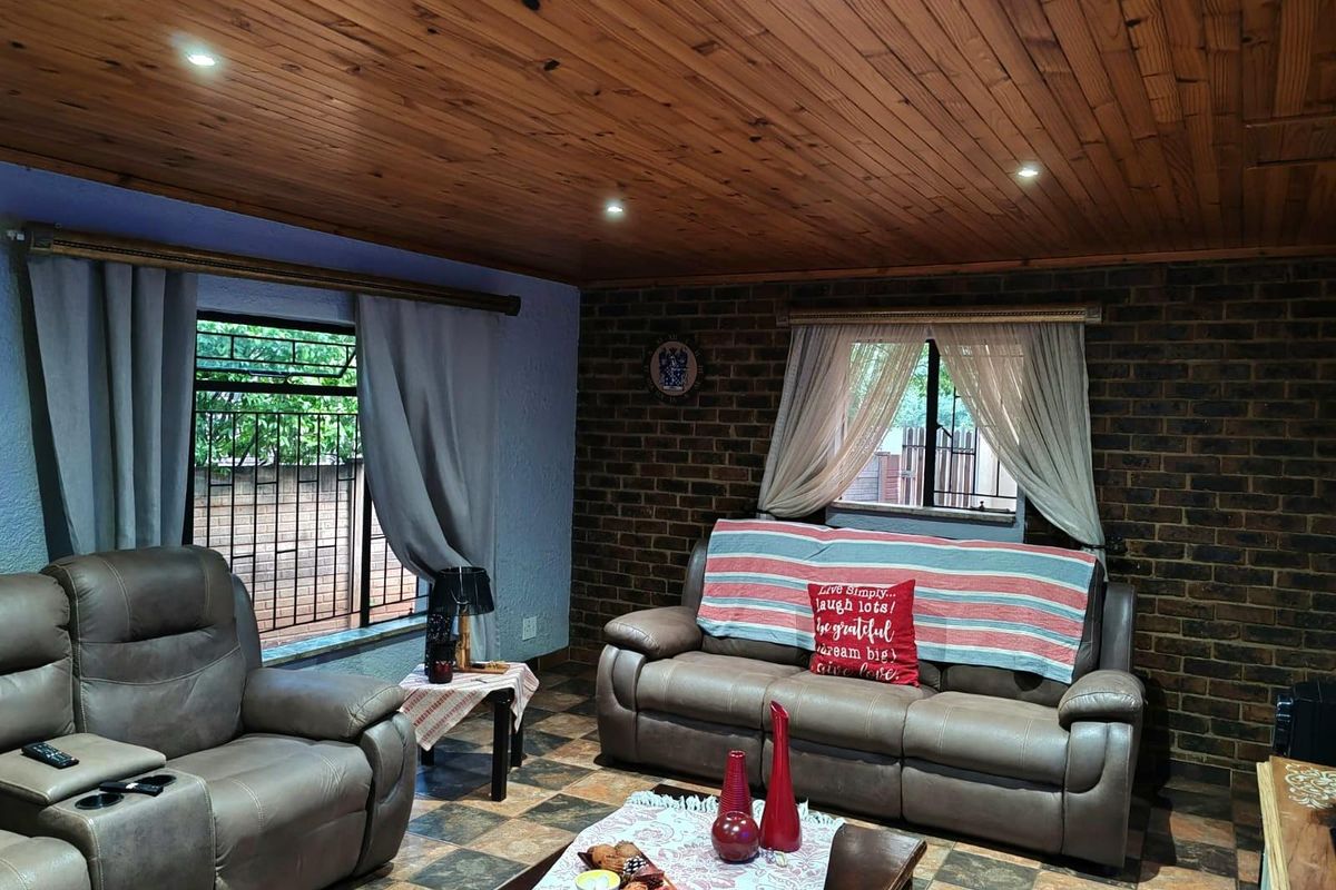 A cozy living room featuring a warm timber ceiling, exposed brick wall, and tiled flooring, providing a rustic and inviting atmosphere.