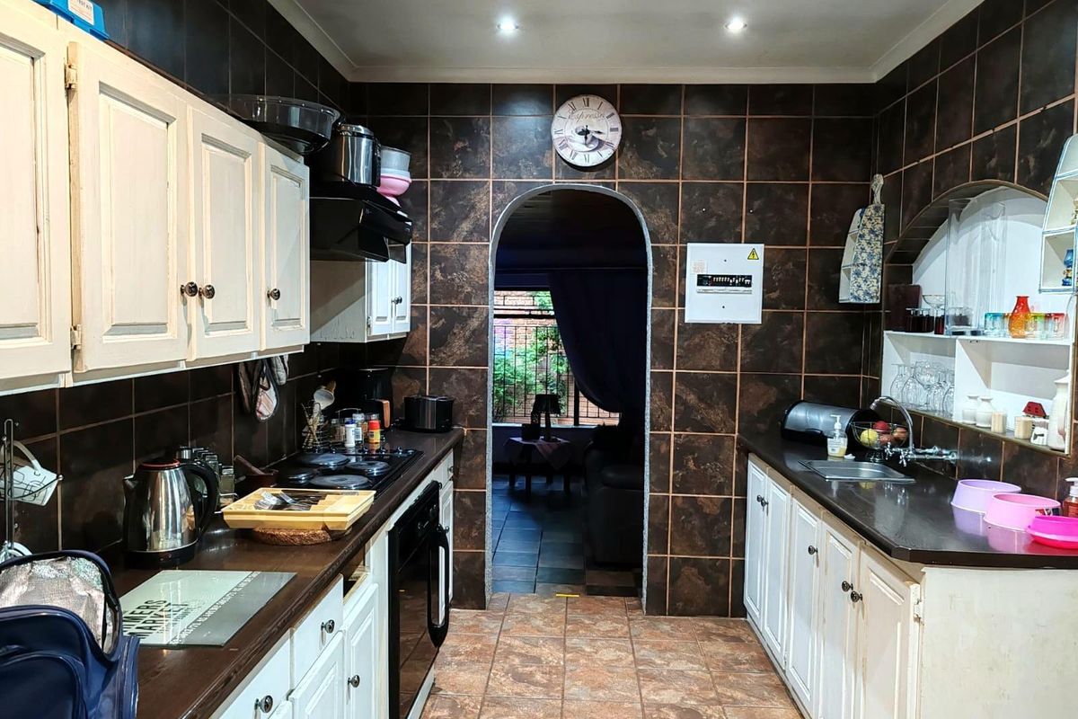 A functional kitchen featuring dark tiled walls, white cabinetry, a gas hob, built-in oven, and an arched doorway leading to the living area.