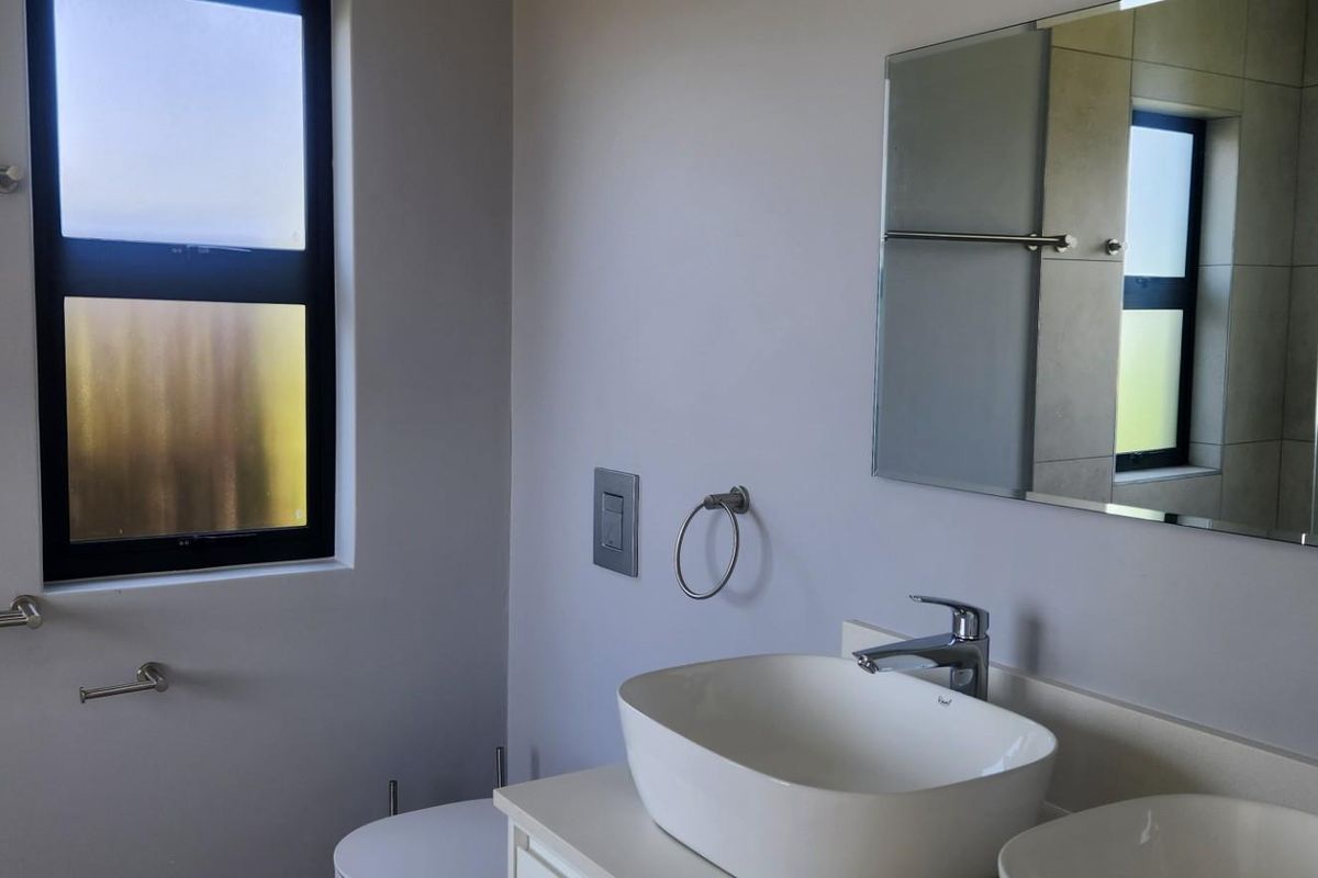 Modern bathroom featuring dual vessel sinks, chrome fixtures, wall-mounted mirrors, and frosted glass windows providing natural light.
