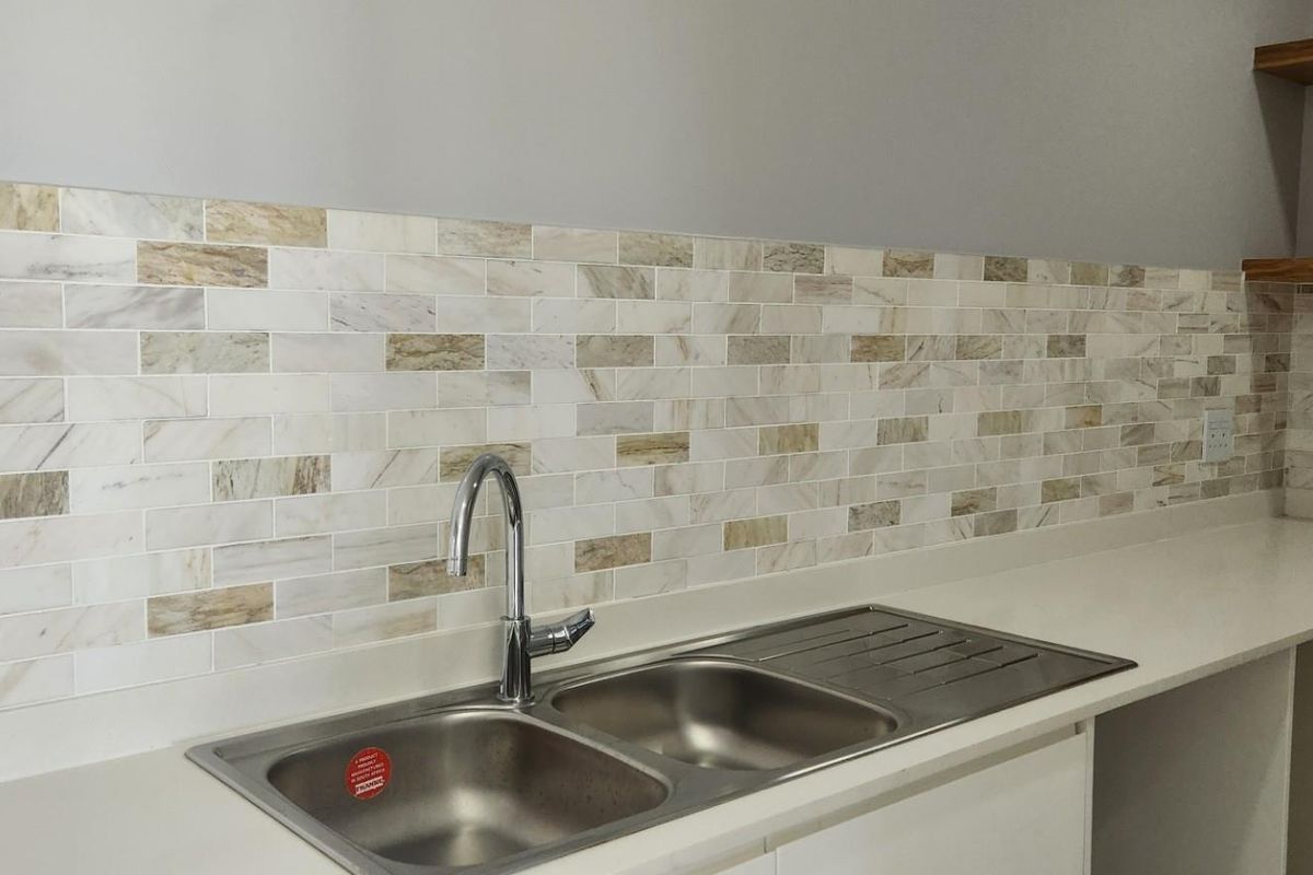 Modern kitchen area featuring a double stainless steel sink, stone-look countertop, and decorative marble-style subway tile backsplash with floating timber shelving.