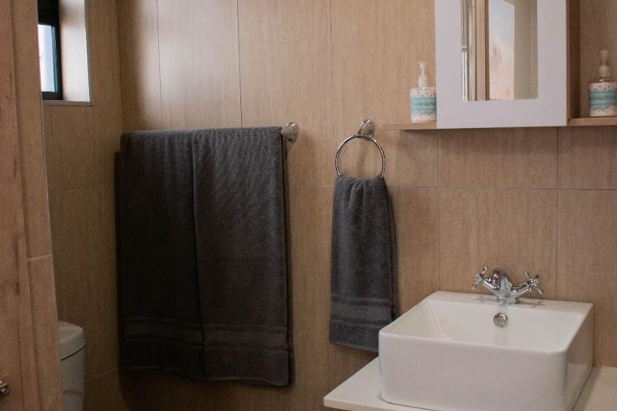A compact, modern bathroom featuring a square vessel sink, wall-mounted vanity cabinet, mirrored medicine cabinet, and a standard toilet with neutral wall tiling.