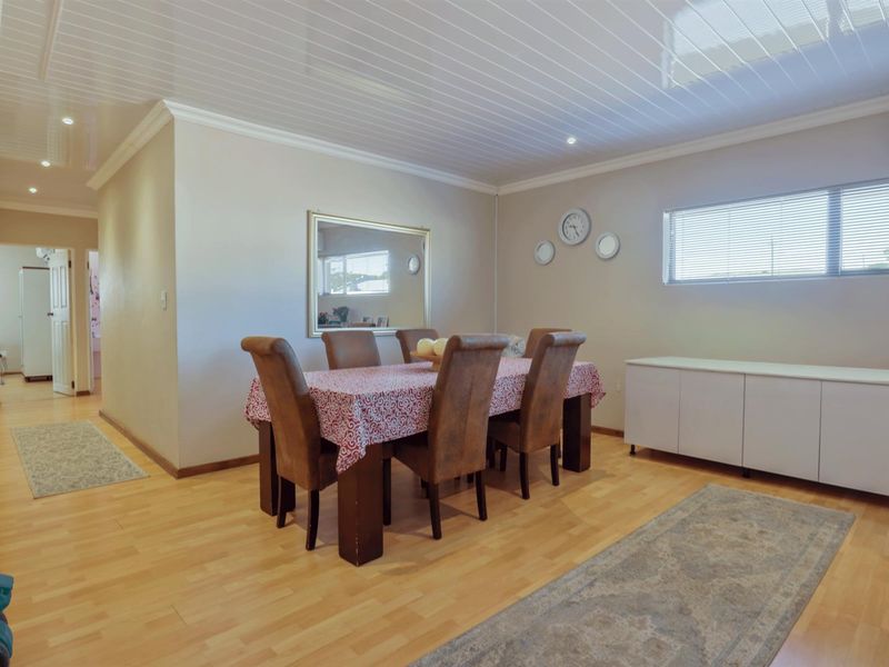 A dining room featuring light wood-look laminate flooring, a glossy white panelled ceiling, and a wall-mounted air conditioning unit.