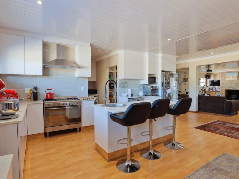 Open-plan kitchen featuring white cabinetry, stainless steel gas stove with extractor fan, and a central island with a prep sink.
