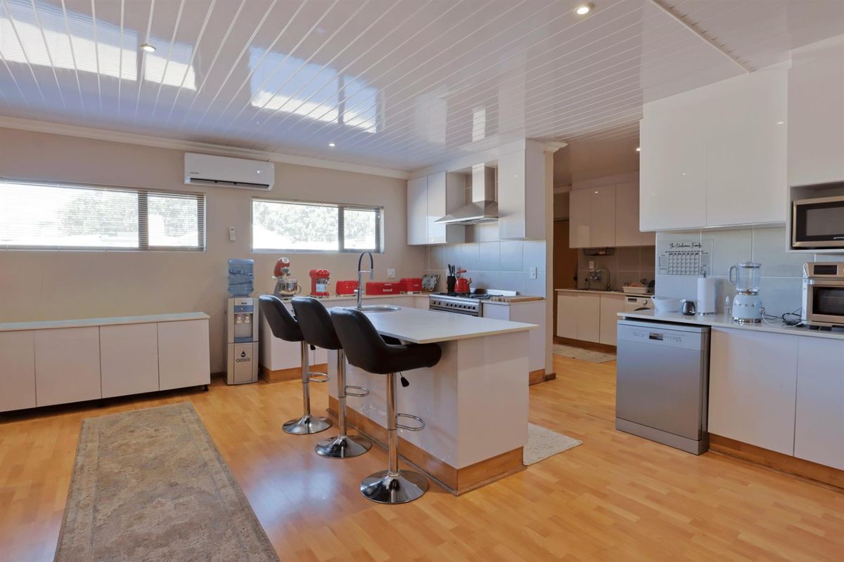 Modern kitchen featuring a central island with breakfast bar, sleek white cabinetry, stainless steel appliances, and light wood-look flooring.