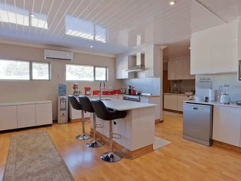 Modern kitchen featuring a central island with breakfast bar, sleek white cabinetry, stainless steel appliances, and light wood-look flooring.