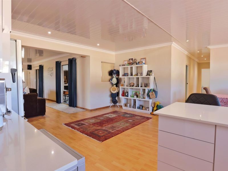 An open-plan living area featuring light wood-look flooring, a glossy white ceiling, and a modern kitchen island, creating a bright and functional living space.