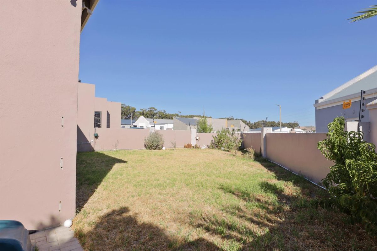 A private rear garden featuring a lawn area enclosed by high perimeter boundary walls.