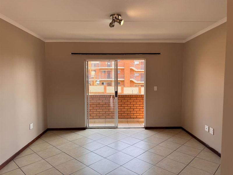 An empty living room featuring neutral walls, ceramic tiled flooring, and a sliding glass door providing access to a balcony.