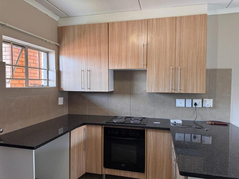 A functional kitchen featuring light wood-grain cabinetry, dark granite countertops, a built-in oven, and an electric hob with tiled splashbacks.