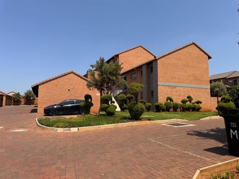 Exterior view of a face brick apartment complex featuring a paved driveway and well-maintained landscaped garden area.