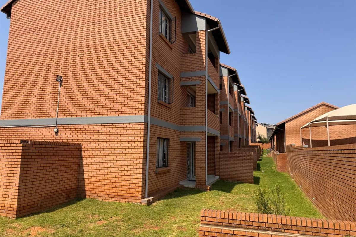 Rear view of a multi-story apartment complex featuring face brick construction, private ground-level access points, and shared lawn areas.