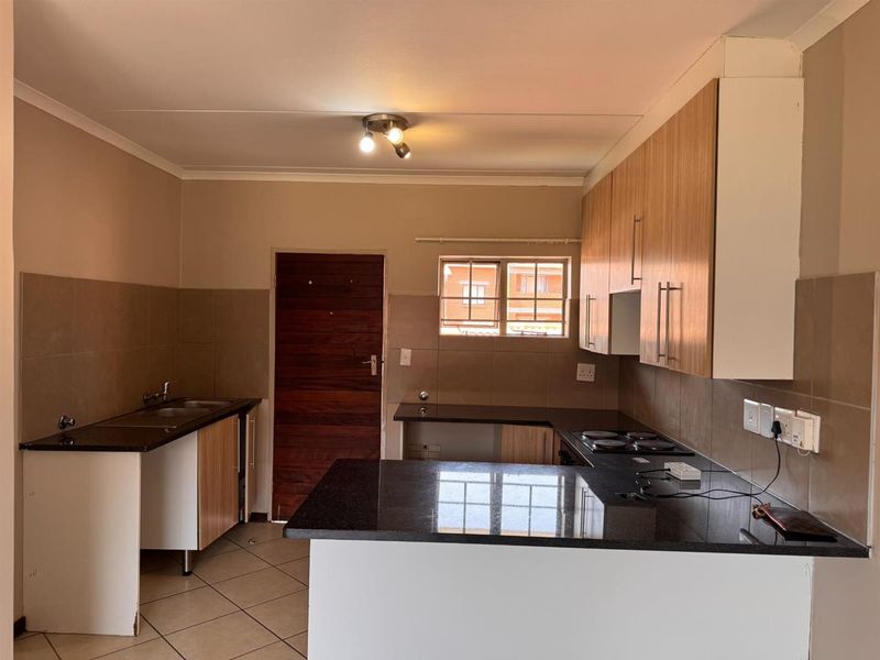 A functional kitchen featuring granite countertops, built-in cabinetry, an electric hob, and a double sink, with tiled flooring and backsplash throughout.
