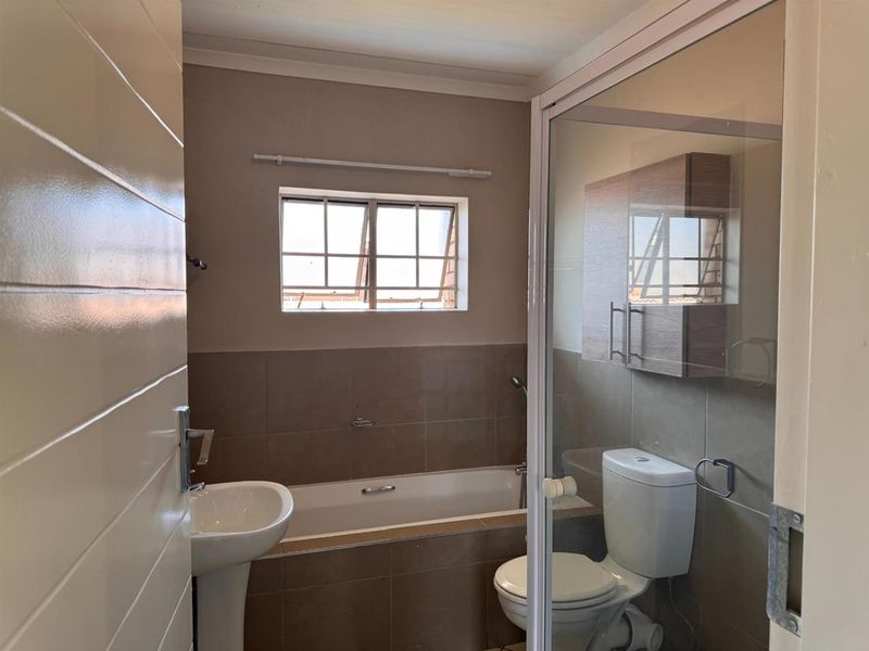 A functional bathroom featuring a pedestal basin, built-in bathtub, separate shower enclosure, and a wall-mounted storage cabinet with neutral wall tiling.