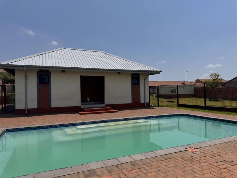 A well-maintained outdoor pool area featuring a swimming pool, brick paved surround, and a detached structure with a metal roof.