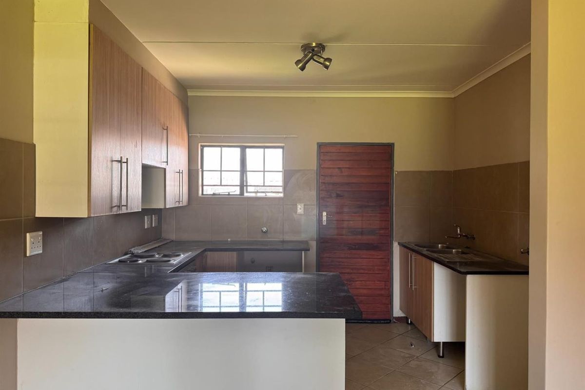A functional kitchen featuring granite countertops, built-in cabinetry, an electric hob, and a double sink, offering a clean and practical layout.