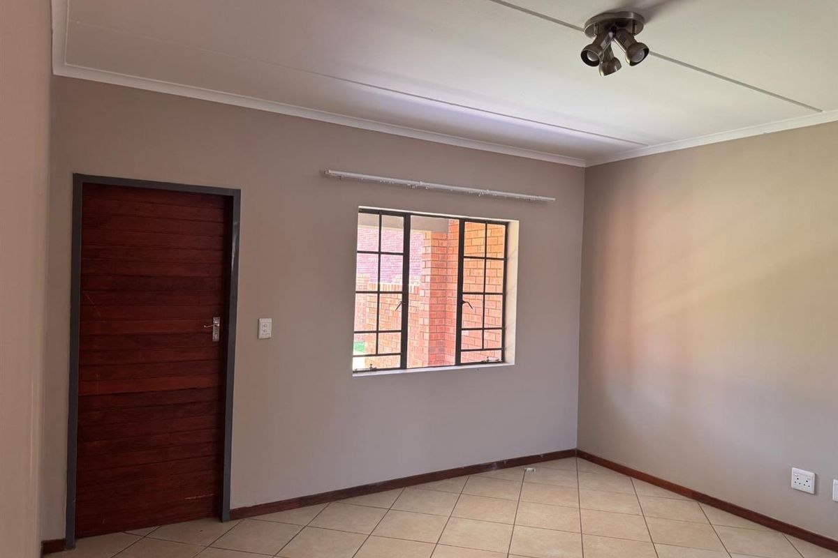 A clean, empty living room featuring neutral wall paint, tiled flooring, and a window with security bars.