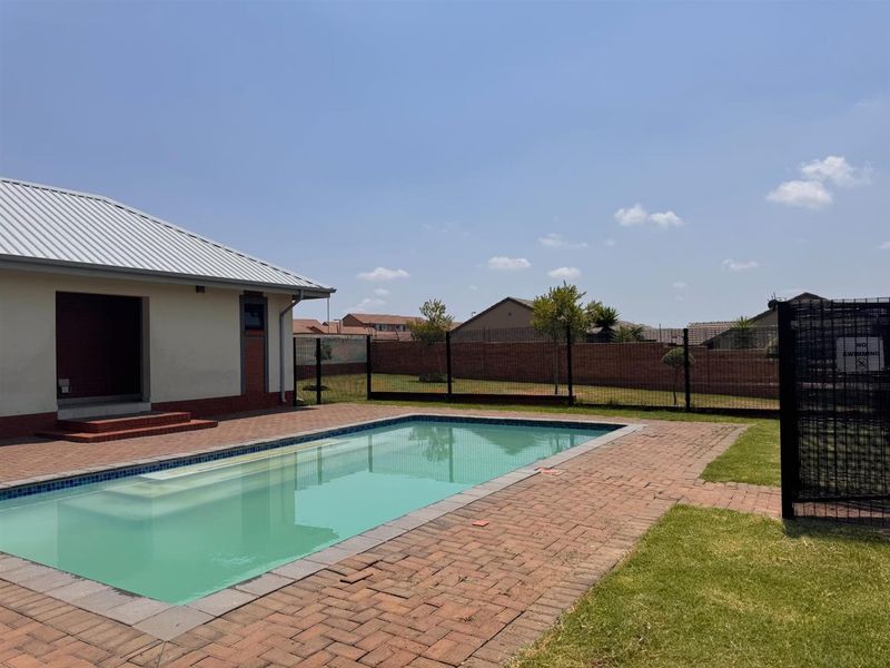 Outdoor pool area featuring a rectangular swimming pool, brick paved surround, and secure metal mesh perimeter fencing.