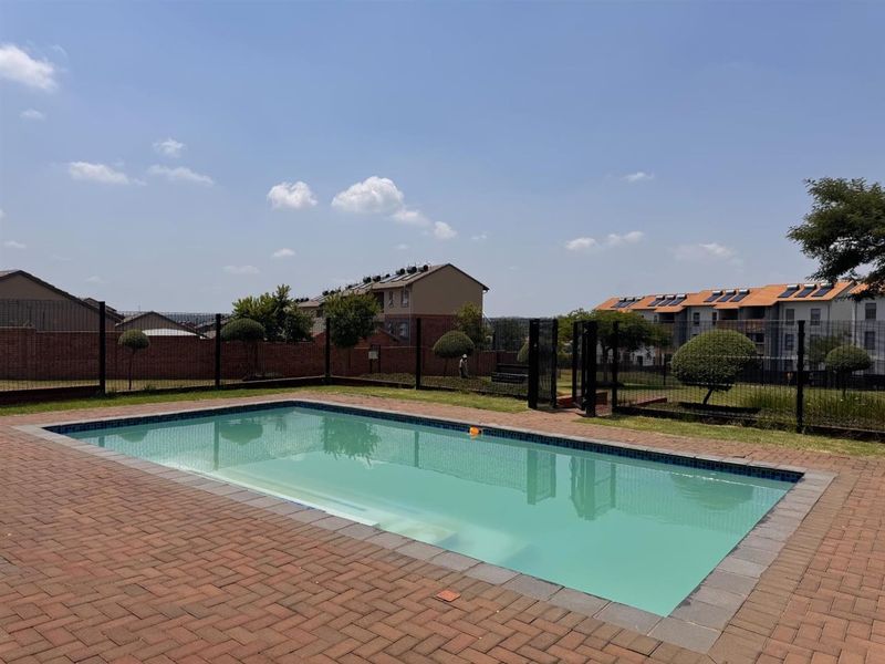 A well-maintained communal swimming pool area featuring brick paving, secure perimeter fencing, and landscaped surroundings within the apartment complex.