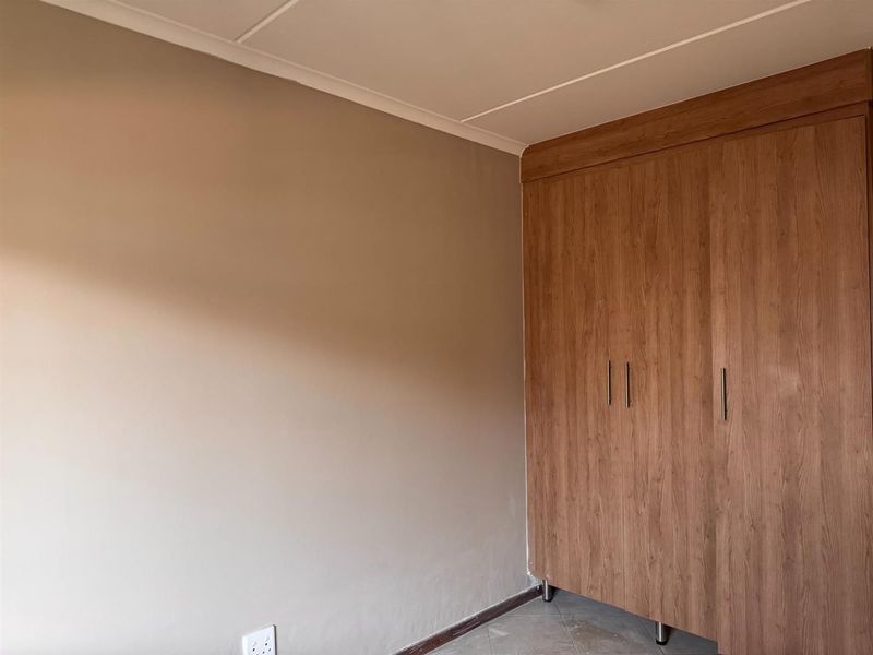 A clean, empty bedroom featuring a modern wood-finish built-in wardrobe and neutral wall tones, providing a versatile space ready for personalization.