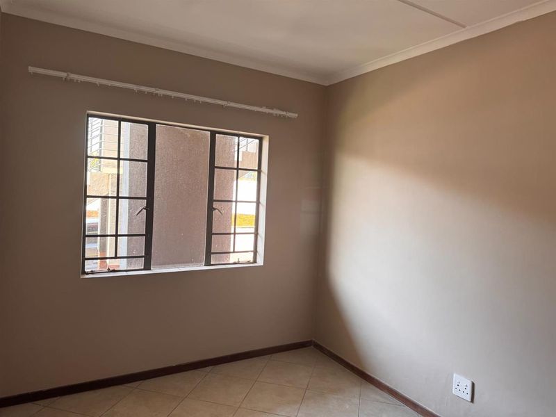An empty bedroom featuring tiled flooring, neutral wall paint, and a metal-framed window with security bars.