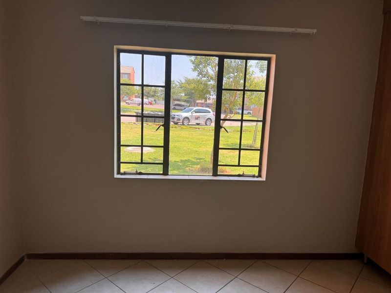 An empty bedroom featuring tiled flooring and a steel-framed window with a view of the exterior grounds.