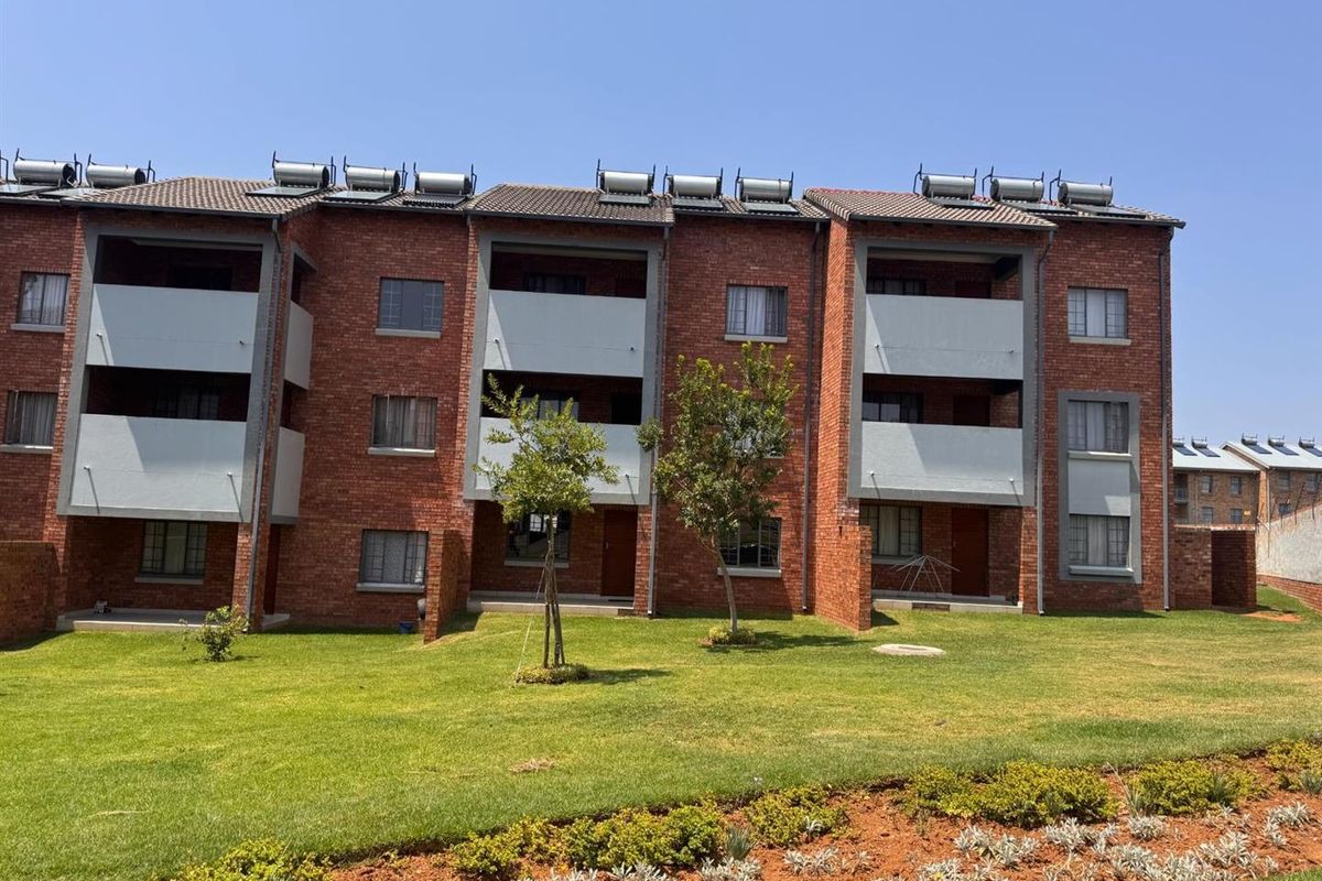 A view of the rear facade of a multi-story apartment complex featuring face brick construction, private balconies, and rooftop solar water heating systems.