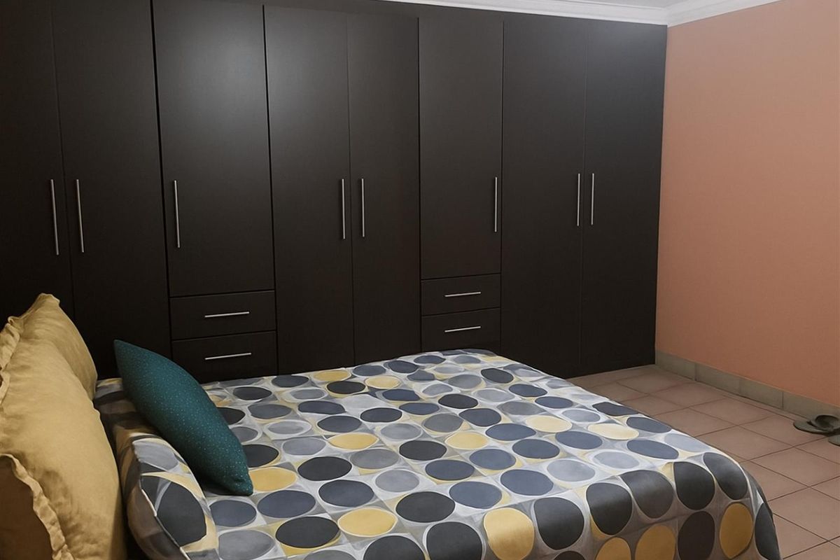 A bedroom featuring extensive floor-to-ceiling built-in dark cabinetry with integrated drawers and tiled flooring.
