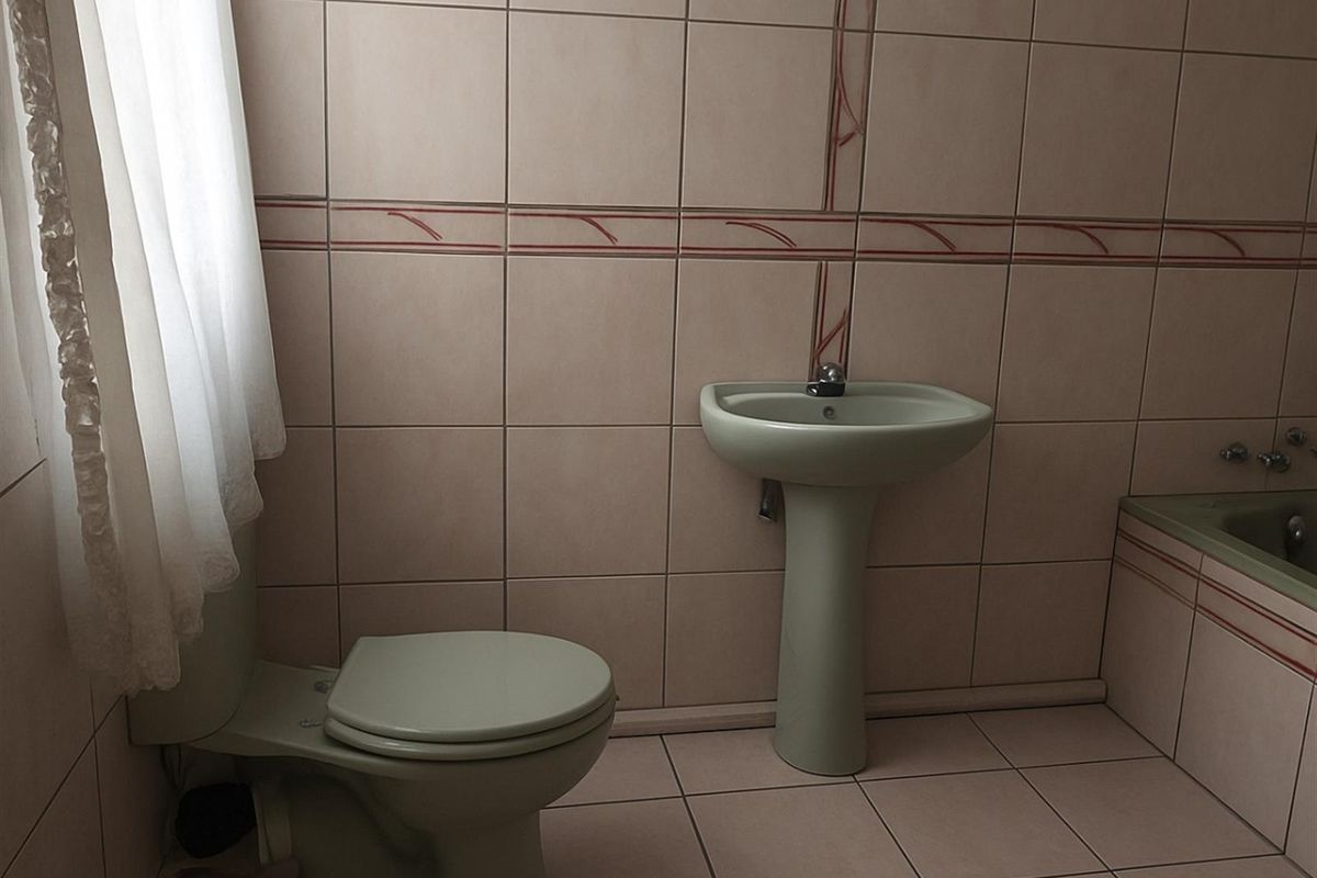A dated bathroom featuring a pedestal basin, toilet, and tiled walls with decorative border accents.