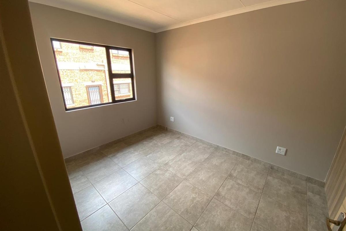A clean, empty bedroom featuring neutral wall paint, tiled flooring, and a window providing natural light.