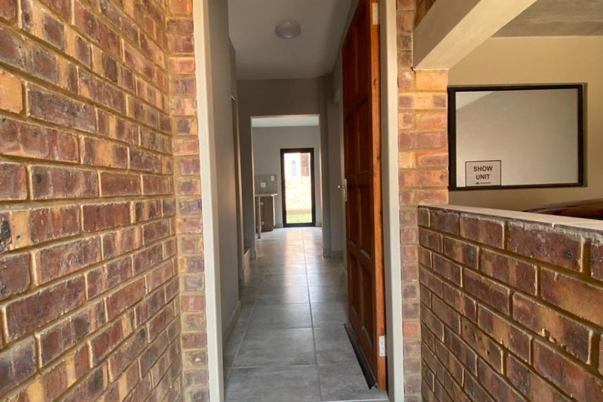 A view of the apartment entrance featuring exposed brickwork, tiled flooring, and a clear line of sight through the hallway to the living area.