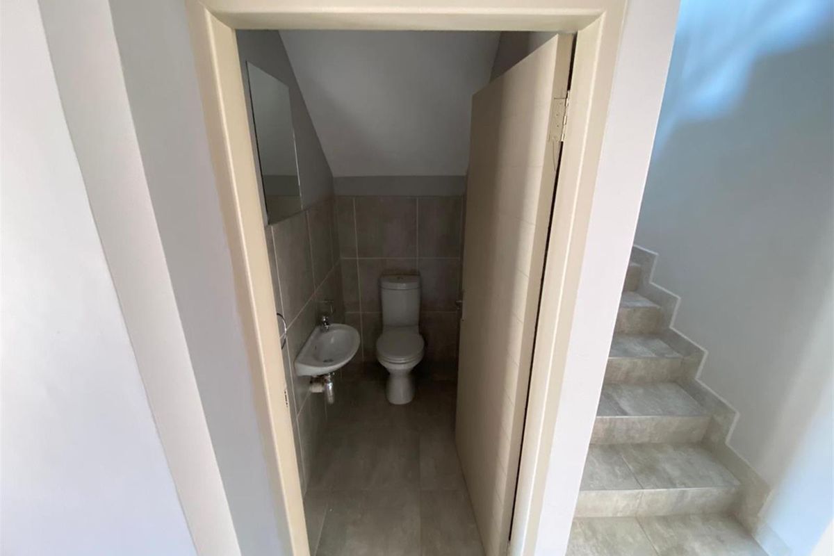 A compact guest bathroom featuring a wall-mounted basin and toilet, finished with neutral floor and wall tiling, located conveniently under the staircase.