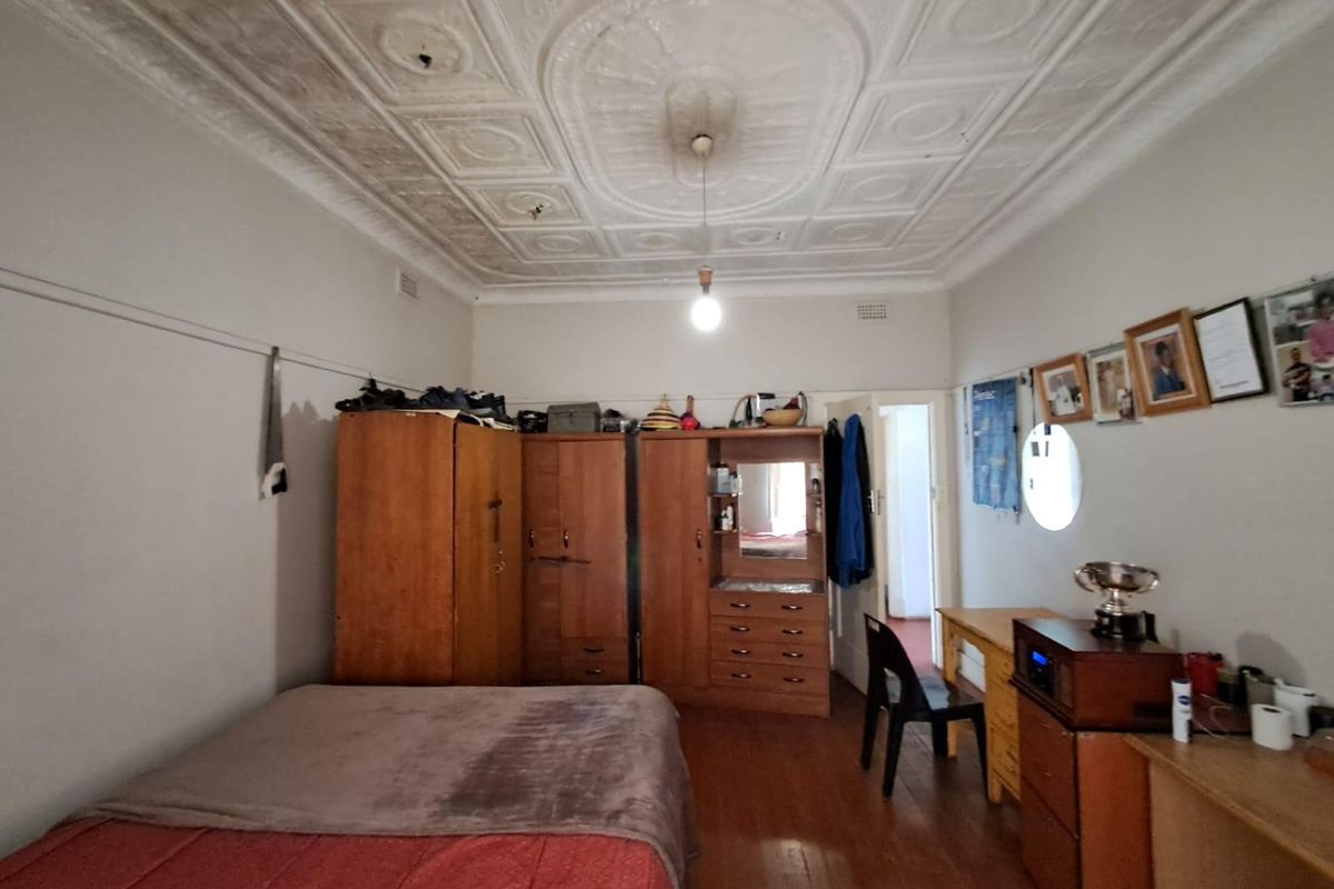 A bedroom featuring original pressed metal ceilings, timber flooring, and a doorway leading to an adjacent room.