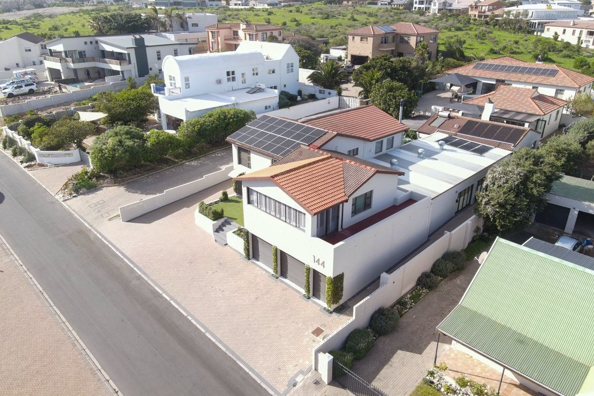 Aerial view of a modern two-story residential property featuring a tiled roof, solar panels, double garage, and paved driveway in a coastal neighborhood.