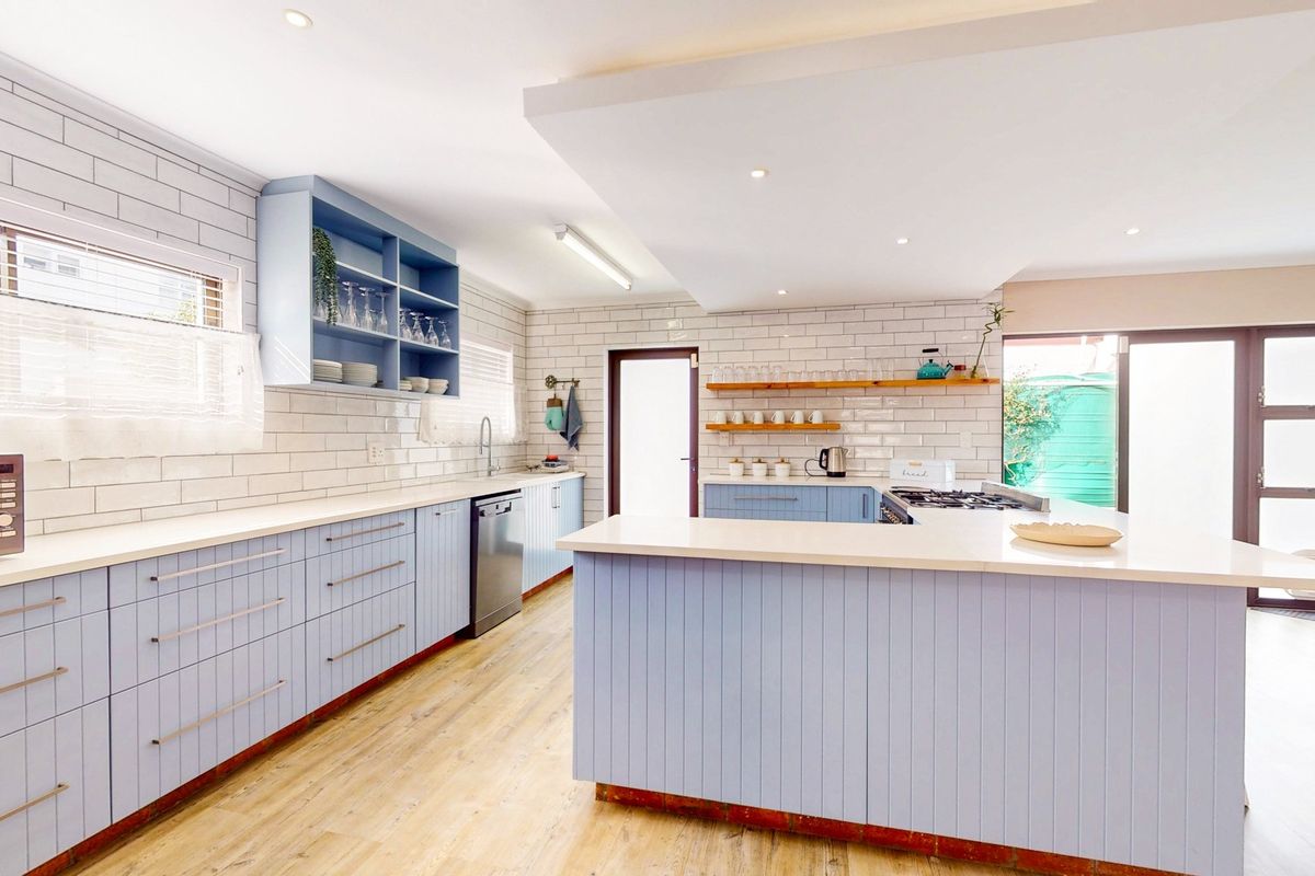 A bright, modern kitchen featuring light blue cabinetry, white subway tile backsplash, stone countertops, and a functional island layout with integrated appliances.