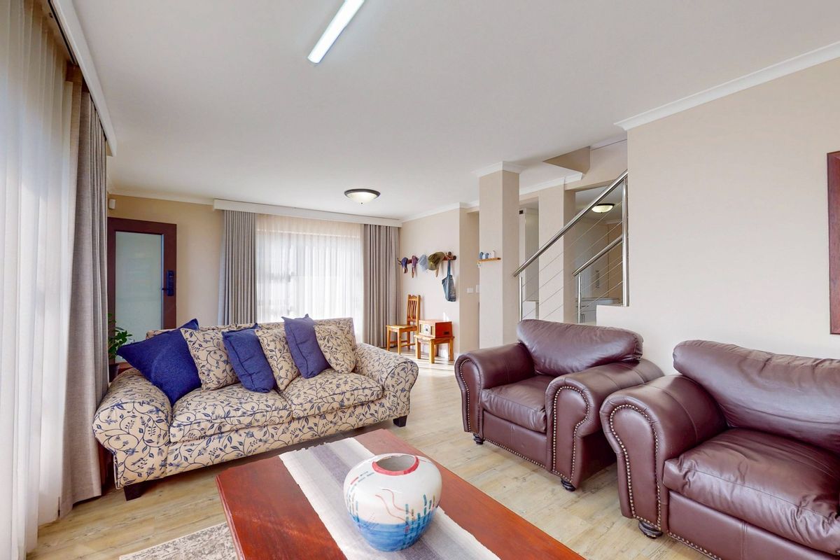 A spacious living room featuring light-toned flooring, a staircase with a modern metal railing, and large windows allowing for ample natural light.