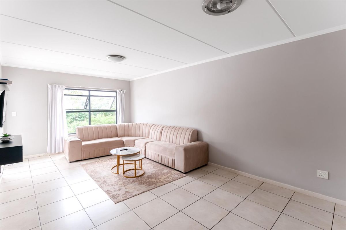 A bright and spacious living room featuring neutral tiled flooring, large windows allowing natural light, and a clean, minimalist aesthetic.