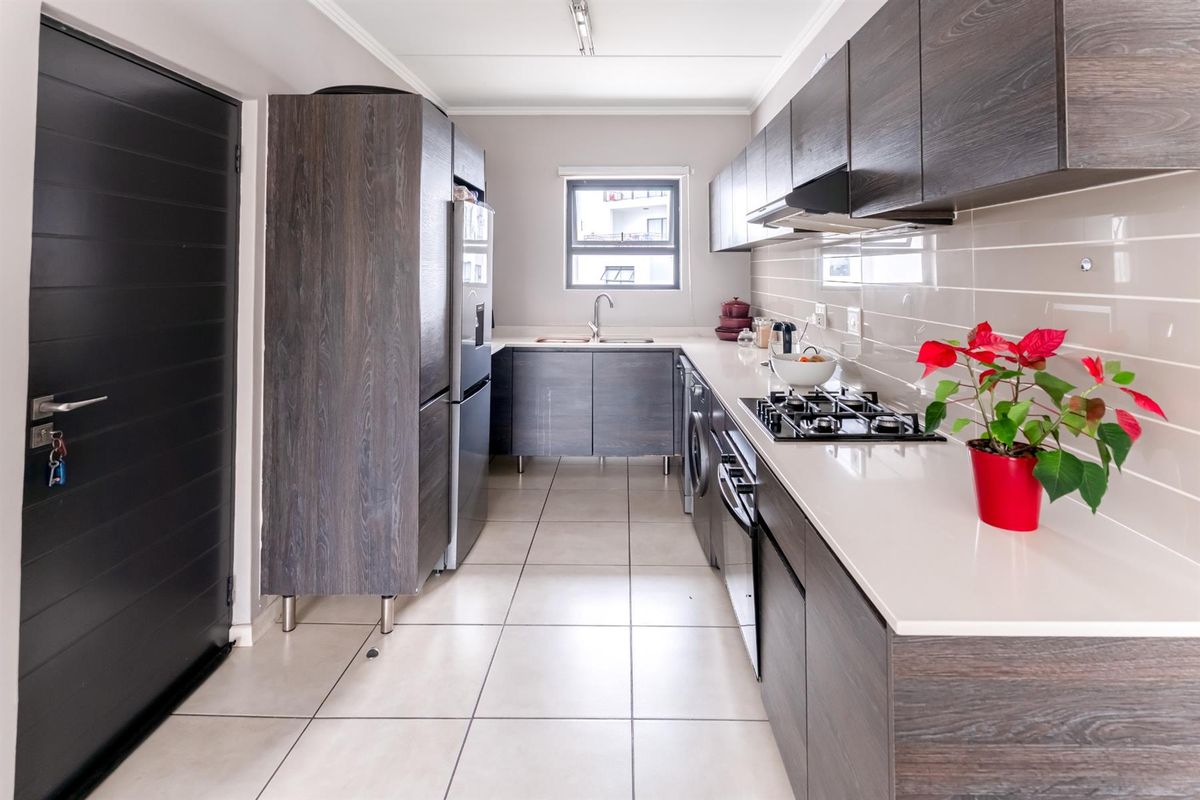 Modern galley-style kitchen featuring dark wood-grain cabinetry, stone countertops, a built-in gas hob, extractor fan, and tiled flooring.