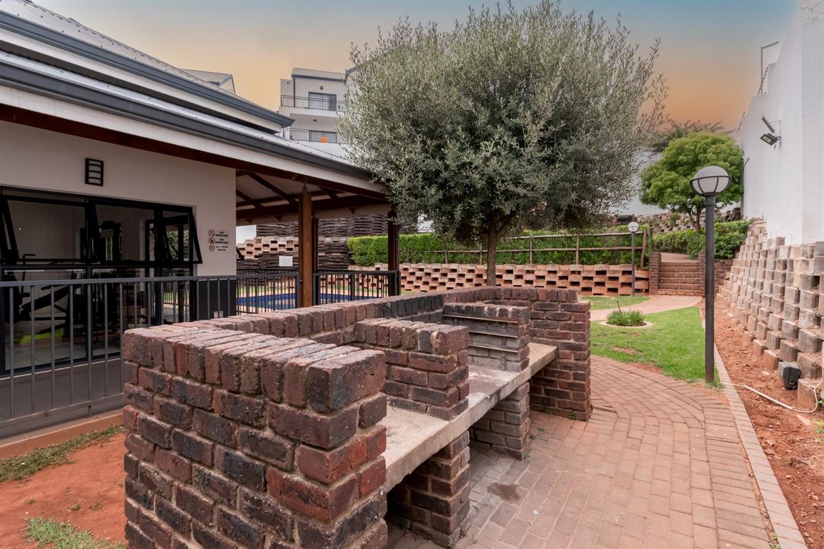 Outdoor communal area featuring a built-in brick braai, paved walkways, and landscaped garden space adjacent to the complex facilities.