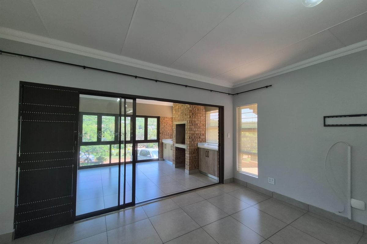 A bright living area featuring large sliding glass doors that open onto a covered patio with a built-in brick braai and tiled flooring.