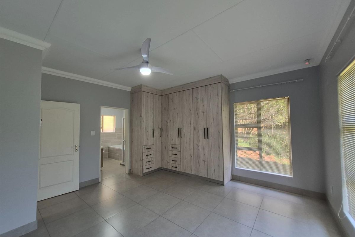 Spacious bedroom featuring built-in wooden cabinetry, tiled flooring, a ceiling fan, and an en-suite bathroom access.