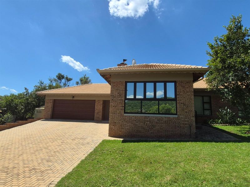 Front exterior view of a face-brick house featuring a paved driveway, double garage, and tiled roof set in a landscaped garden.