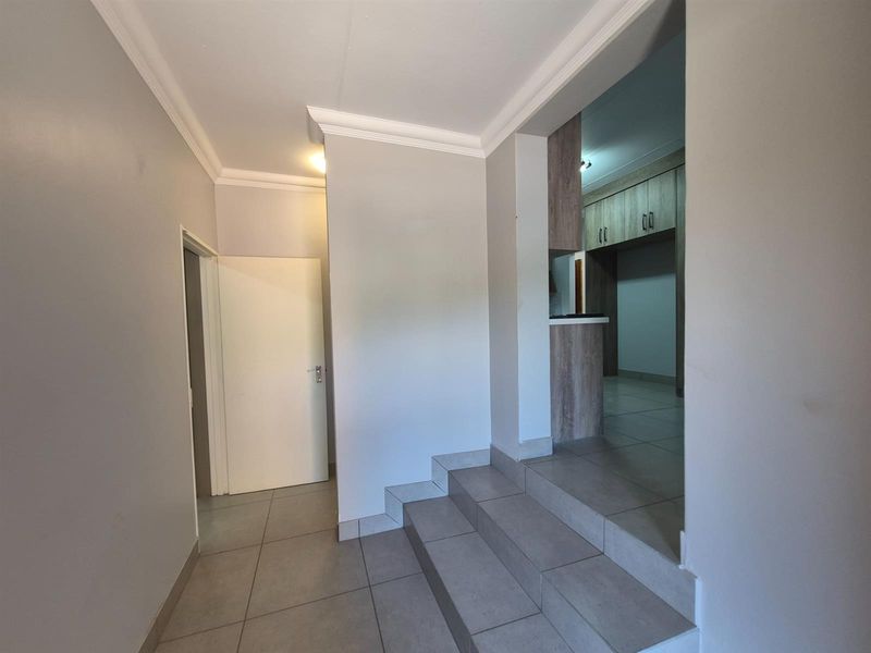 An interior view of a hallway featuring tiled flooring, a small staircase leading to an adjacent room, and crown molding details.