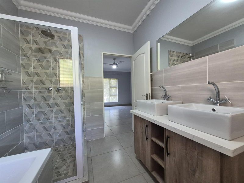 Modern bathroom featuring a double vanity with vessel sinks, a glass-enclosed shower with decorative tiling, and neutral floor tiles.