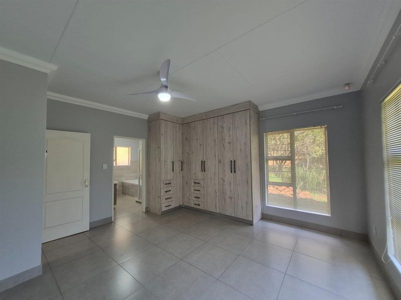 Spacious bedroom featuring built-in wooden cabinetry, tiled flooring, a ceiling fan, and an en-suite bathroom access.