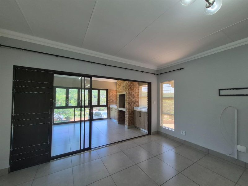 A bright living area featuring large sliding glass doors that open onto a covered patio with a built-in brick braai and tiled flooring.